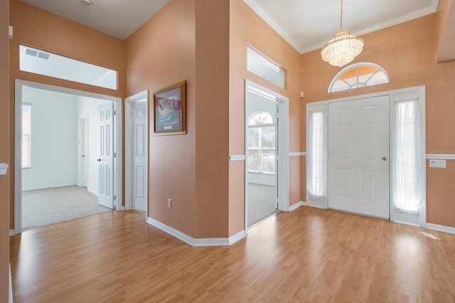 entrance foyer featuring an inviting chandelier, light wood-type flooring, a high ceiling, and ornamental molding