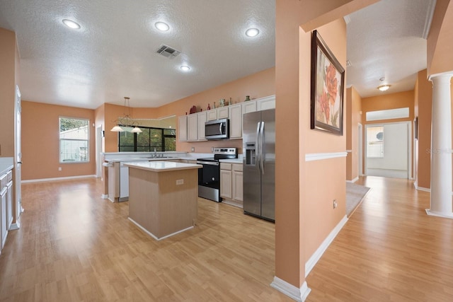 kitchen featuring appliances with stainless steel finishes, a center island, white cabinetry, sink, and hanging light fixtures