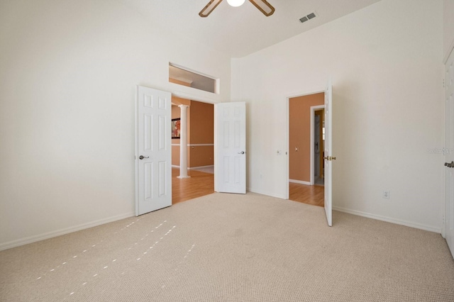 unfurnished bedroom with ceiling fan, a towering ceiling, and light carpet