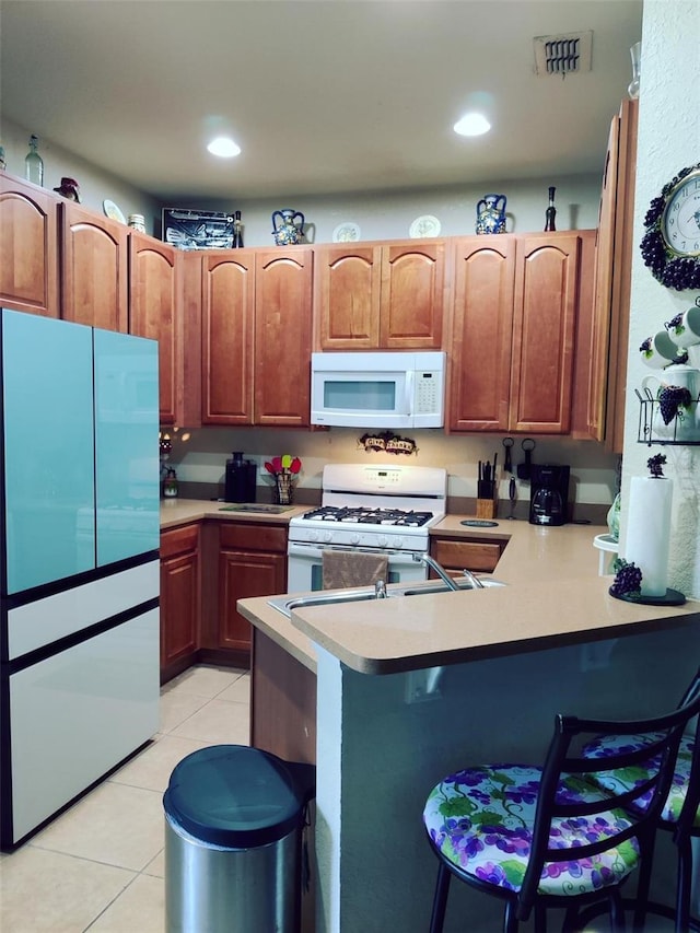 kitchen with a breakfast bar, white appliances, light tile patterned floors, and kitchen peninsula