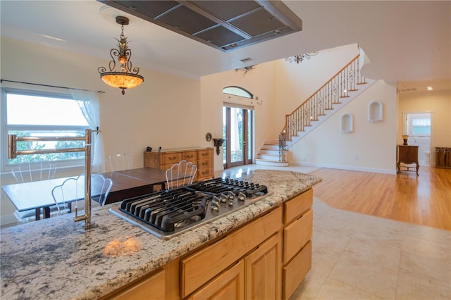 kitchen with pendant lighting, light tile patterned floors, light stone counters, ornamental molding, and stainless steel gas cooktop