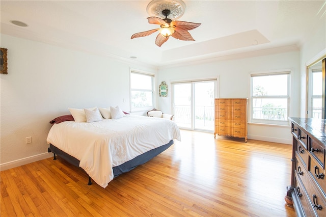 bedroom with light hardwood / wood-style floors, access to outside, ceiling fan, and a tray ceiling