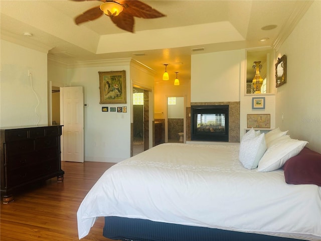 bedroom featuring hardwood / wood-style flooring, ornamental molding, ceiling fan, and a tray ceiling