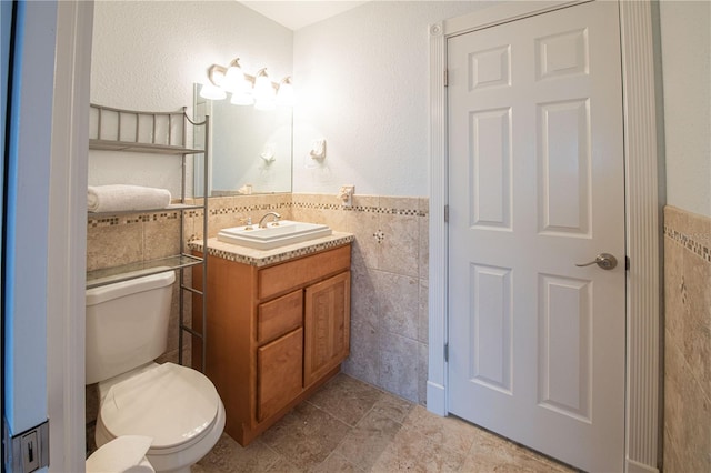 bathroom with vanity, toilet, and tile walls