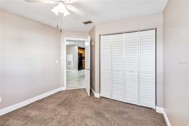 unfurnished bedroom featuring light colored carpet, ceiling fan, black fridge, a textured ceiling, and a closet