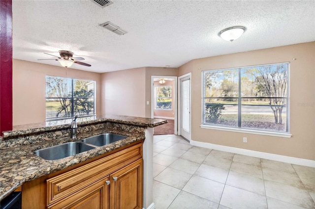 kitchen with sink, dishwasher, ceiling fan, a textured ceiling, and dark stone counters