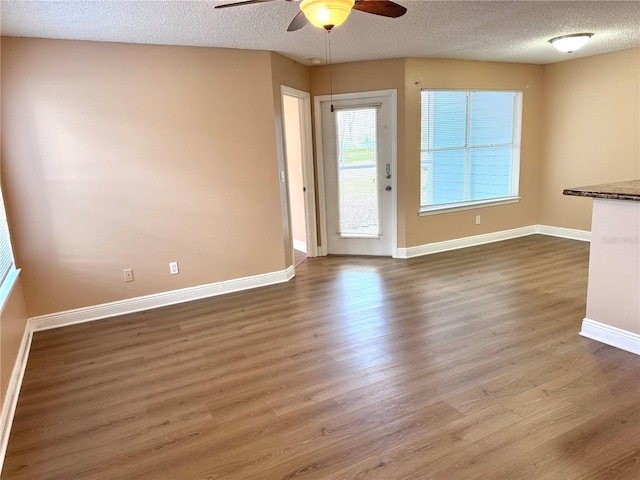 unfurnished living room featuring a ceiling fan, a textured ceiling, baseboards, and wood finished floors