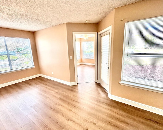 spare room featuring a textured ceiling, light wood-type flooring, and baseboards