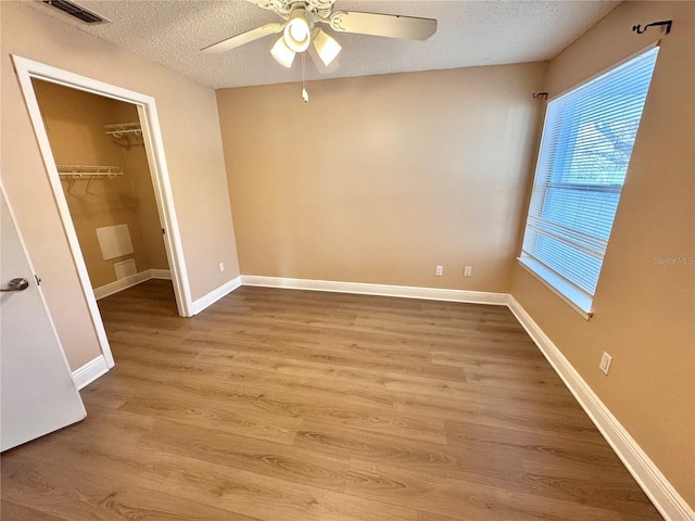 unfurnished bedroom featuring visible vents, a spacious closet, a textured ceiling, wood finished floors, and baseboards