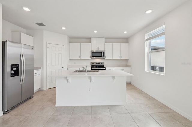 kitchen with a kitchen island with sink, a sink, white cabinets, light countertops, and appliances with stainless steel finishes