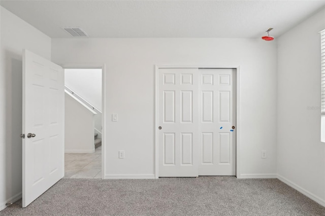 unfurnished bedroom featuring light colored carpet, a closet, visible vents, and baseboards