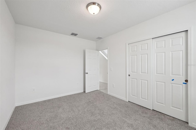 unfurnished bedroom featuring a textured ceiling, light carpet, visible vents, baseboards, and a closet