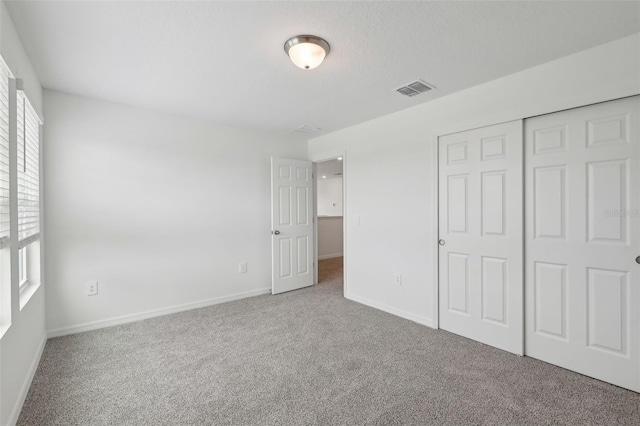 unfurnished bedroom with a textured ceiling, visible vents, baseboards, a closet, and carpet