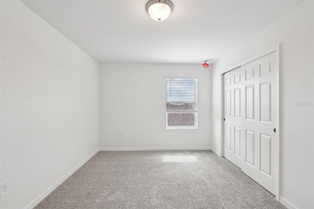 unfurnished bedroom featuring a closet, light colored carpet, a textured ceiling, and baseboards