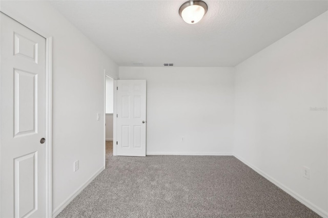 empty room featuring carpet, visible vents, a textured ceiling, and baseboards