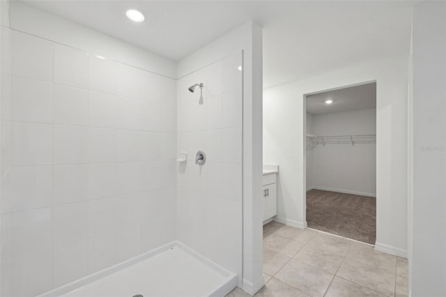 bathroom with tile patterned flooring, a spacious closet, tiled shower, and vanity