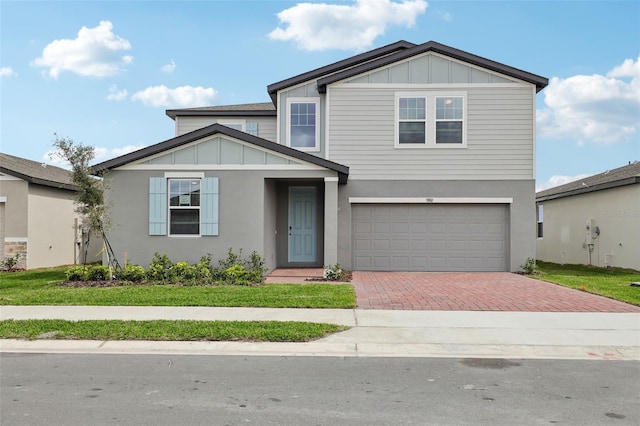 view of front of property featuring board and batten siding, decorative driveway, a front lawn, and an attached garage