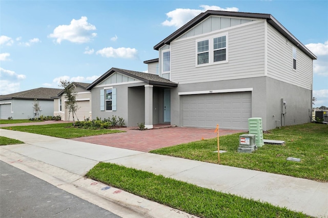 view of front of property featuring decorative driveway, stucco siding, board and batten siding, a front yard, and a garage