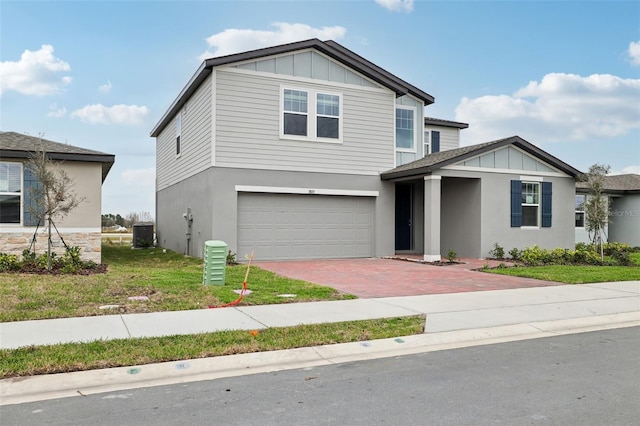 view of front facade with decorative driveway, an attached garage, board and batten siding, cooling unit, and a front lawn