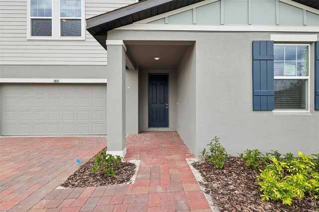 entrance to property featuring a garage, decorative driveway, and stucco siding