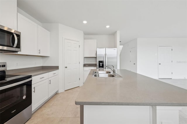 kitchen with light tile patterned floors, stainless steel appliances, white cabinets, a kitchen island with sink, and a sink