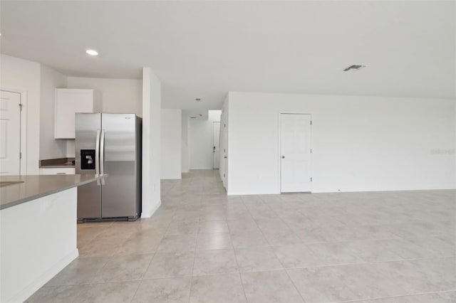 kitchen with light tile patterned floors, dark countertops, visible vents, white cabinets, and stainless steel fridge with ice dispenser