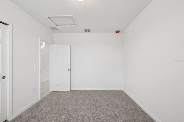 carpeted spare room with attic access, visible vents, and baseboards