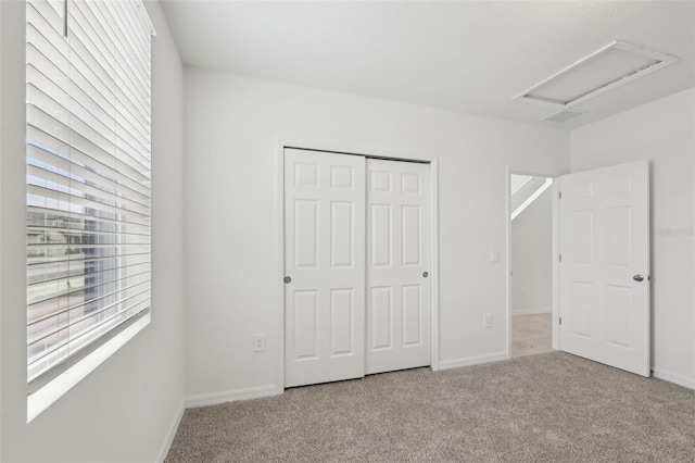 unfurnished bedroom with carpet floors, a closet, visible vents, attic access, and baseboards