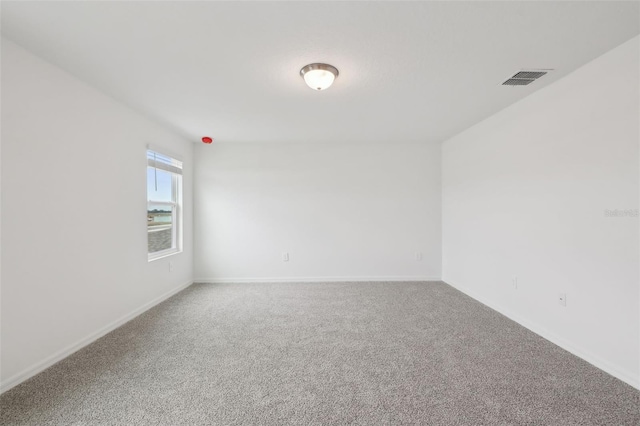 empty room with carpet, visible vents, and baseboards