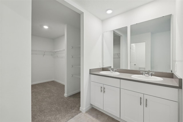 bathroom featuring double vanity, a sink, a walk in closet, and baseboards