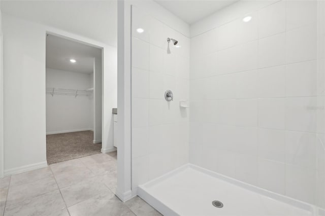 full bath with a walk in closet, baseboards, a tile shower, and tile patterned floors