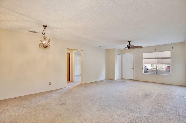 carpeted empty room featuring ceiling fan with notable chandelier and a textured ceiling