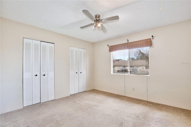 unfurnished bedroom with multiple closets, ceiling fan, light colored carpet, and a textured ceiling