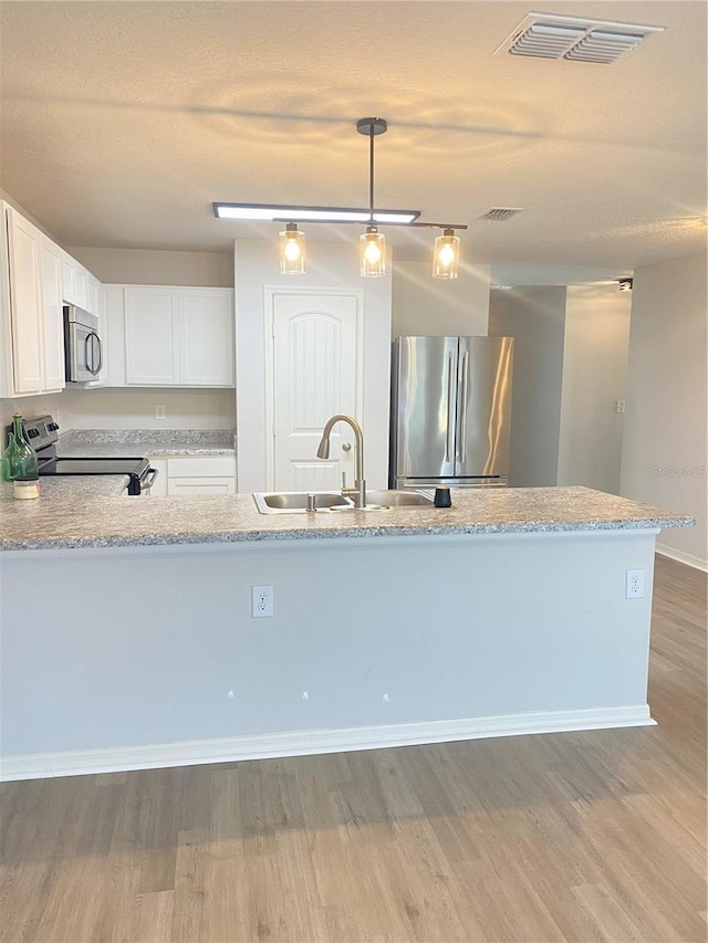 kitchen featuring visible vents, white cabinets, wood finished floors, stainless steel appliances, and a sink