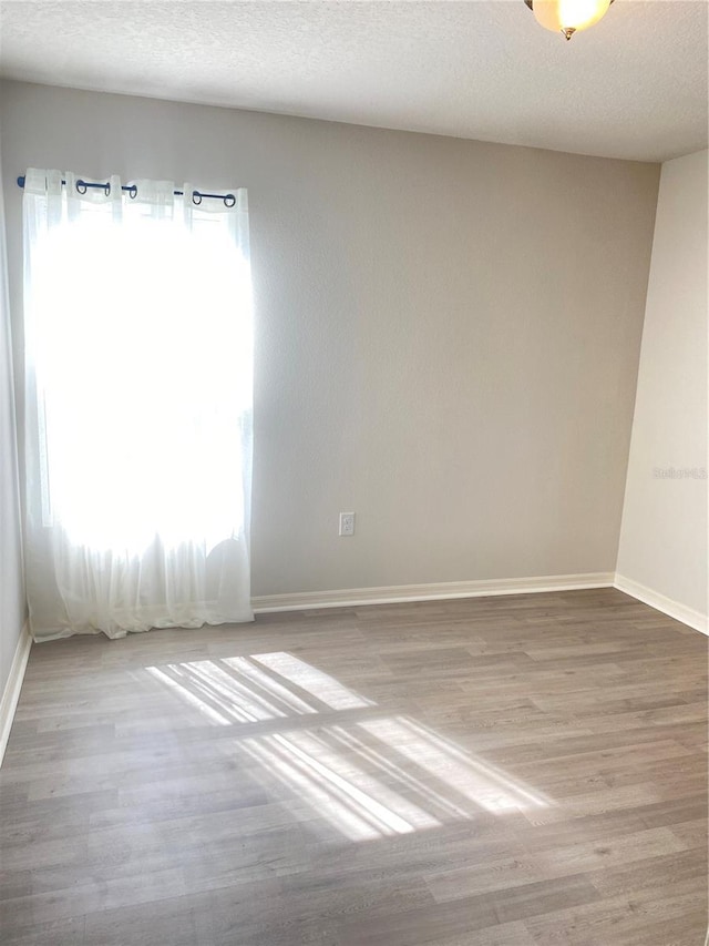 unfurnished room with a textured ceiling, baseboards, and wood finished floors