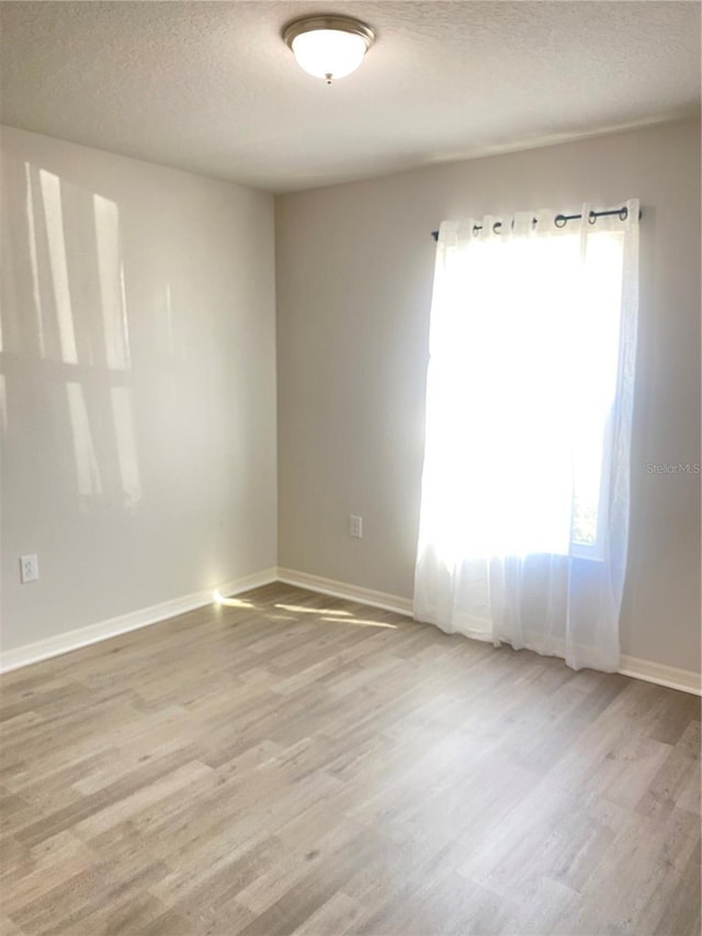 spare room with baseboards, a textured ceiling, and light wood finished floors