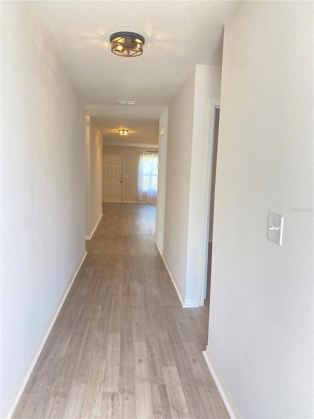 corridor featuring a textured ceiling, light wood-type flooring, visible vents, and baseboards