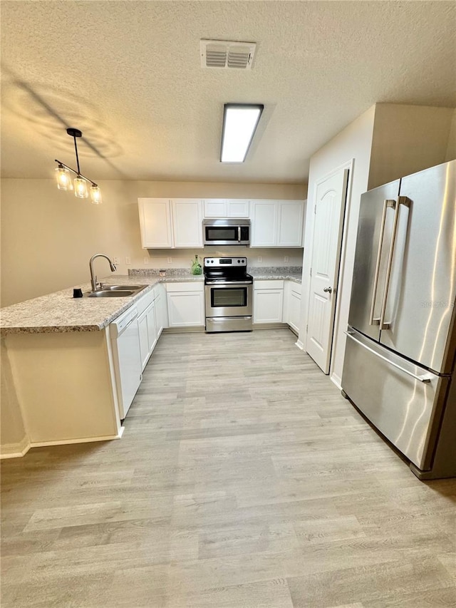 kitchen with stainless steel appliances, a peninsula, a sink, visible vents, and light wood finished floors