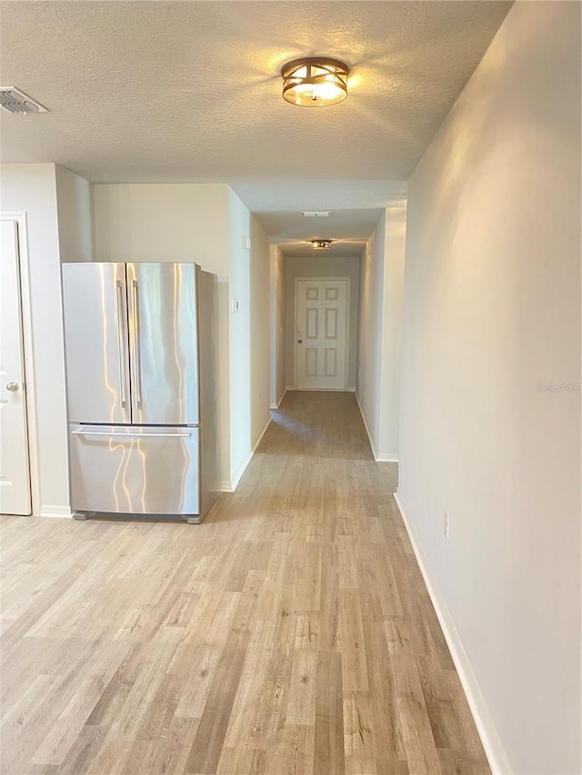 hallway featuring light wood-style flooring, baseboards, and a textured ceiling