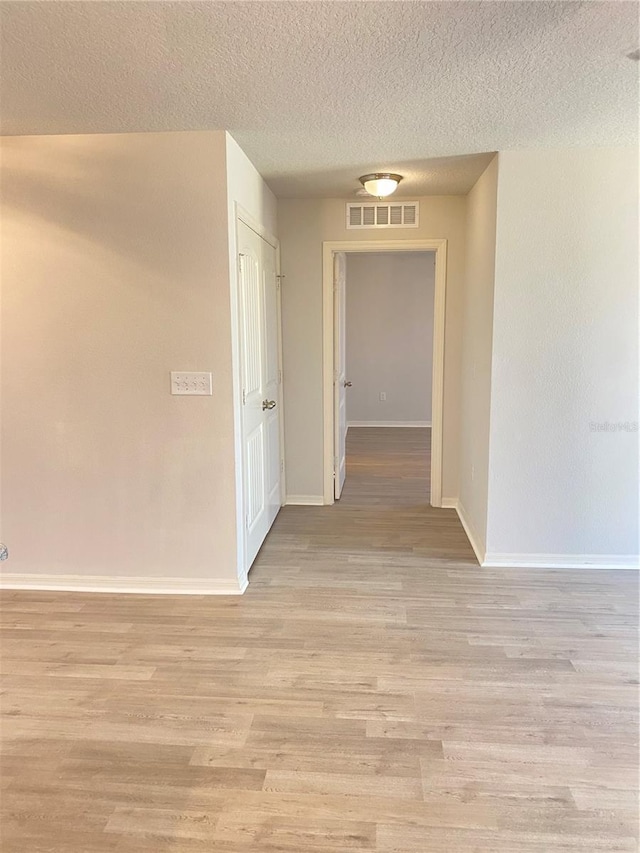 hallway featuring a textured ceiling, baseboards, visible vents, and light wood-style floors