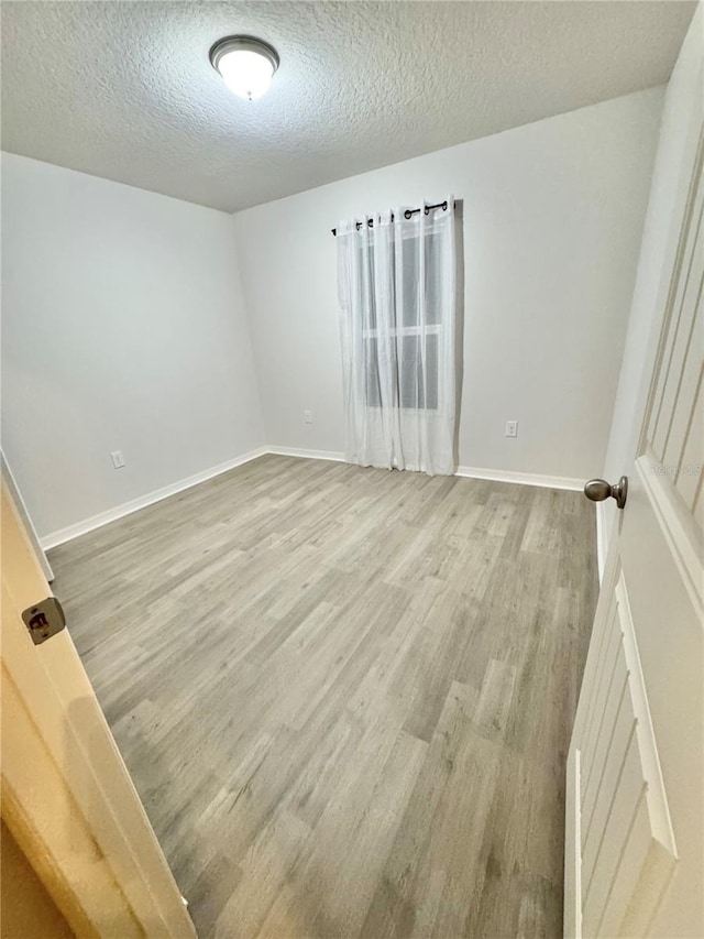 empty room with a textured ceiling, light wood finished floors, and baseboards