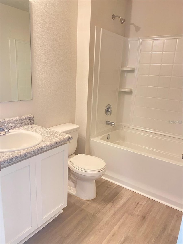 full bathroom with a textured wall, toilet, wood finished floors, vanity, and bathing tub / shower combination