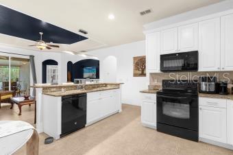 kitchen featuring visible vents, a kitchen island, ceiling fan, black appliances, and white cabinetry