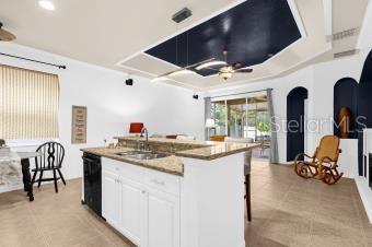 kitchen featuring a ceiling fan, an island with sink, a sink, white cabinets, and black dishwasher