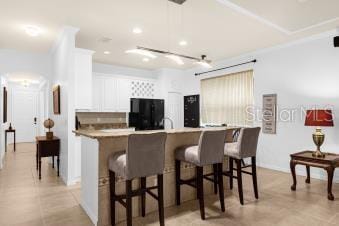 kitchen featuring a kitchen bar, a kitchen island with sink, black refrigerator, white cabinets, and light countertops