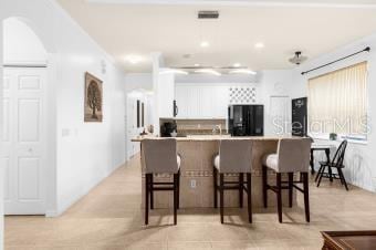 kitchen featuring a kitchen bar, refrigerator, visible vents, and white cabinetry