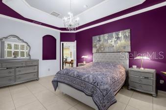 bedroom featuring tile patterned floors, visible vents, an inviting chandelier, a raised ceiling, and an accent wall