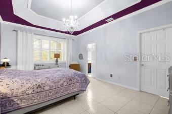 bedroom featuring a tray ceiling, crown molding, light tile patterned floors, baseboards, and a chandelier