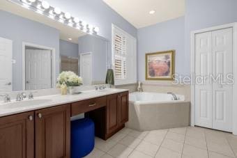 full bath with tile patterned flooring, double vanity, a bath, and a sink