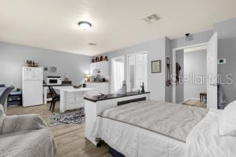 bedroom featuring visible vents, light wood-type flooring, and freestanding refrigerator